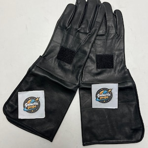 May include: A pair of black leather gloves with long cuffs. Each glove has a black Velcro patch on the back of the hand and a white label with the text "Galactic Props" and a logo.