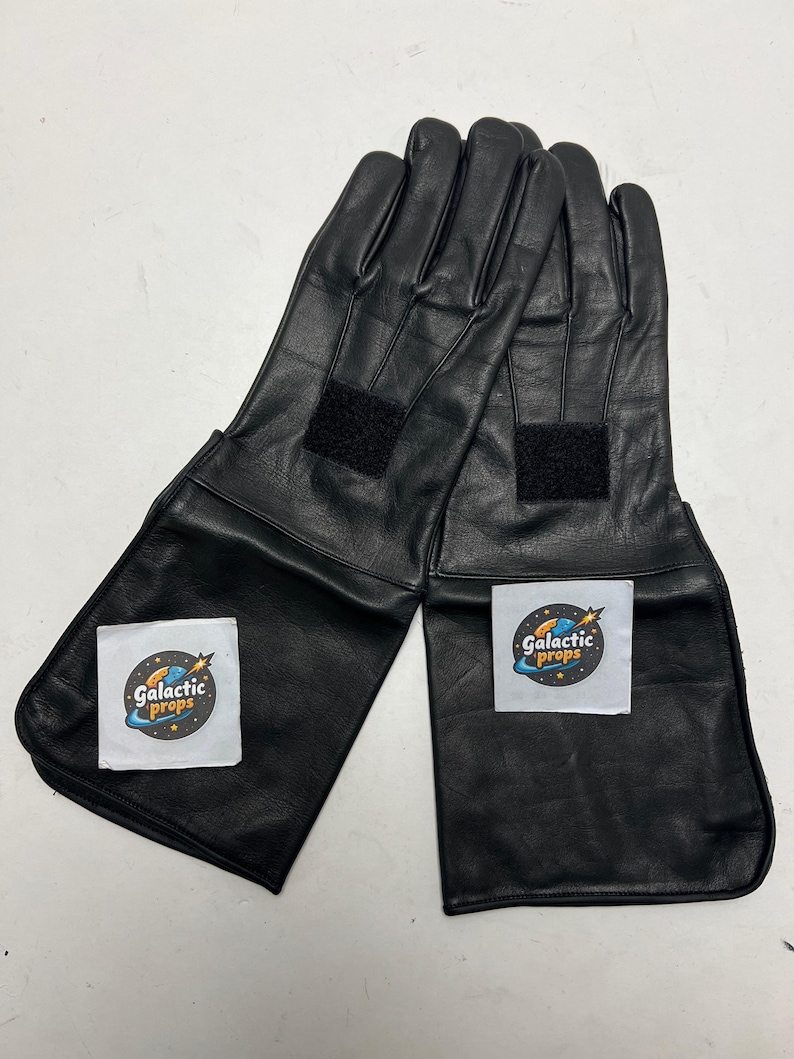 May include: A pair of black leather gloves with long cuffs. Each glove has a black Velcro patch on the back of the hand and a white label with the text "Galactic Props" and a logo.