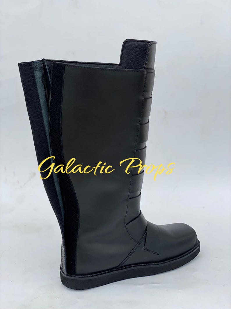 May include: A black knee-high boot with a flat sole. The boot features a side zipper, decorative straps, and the text "Galactic Props" in gold script. The boot is made of a smooth, matte material.