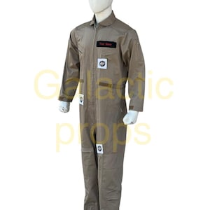 Könnte beinhalten: Beigefarbener Overall mit mehreren Aufnähern und einem schwarzen Namensschild mit der Aufschrift "Your Name". Der Overall hat einen Reißverschluss, mehrere Taschen und wird auf einer Schaufensterpuppe präsentiert. Das Design deutet auf ein Kostüm oder eine Uniform hin.