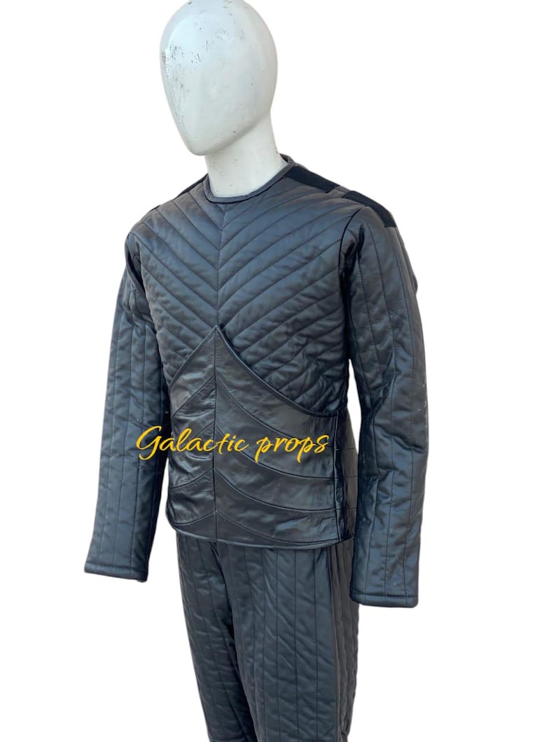 Puede incluir: Mono negro acolchado con un patr&oacute;n de diamante. El mono tiene mangas largas y cuello redondo. El texto "Galactic Props" est&aacute; bordado en la parte delantera del mono.