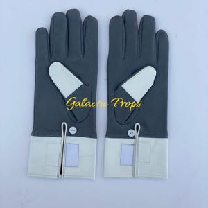 May include: A pair of gray gloves with white accents. The gloves have a white cuff and a white patch on the back of the hand. The text "Galactic Props" is printed on the gloves.