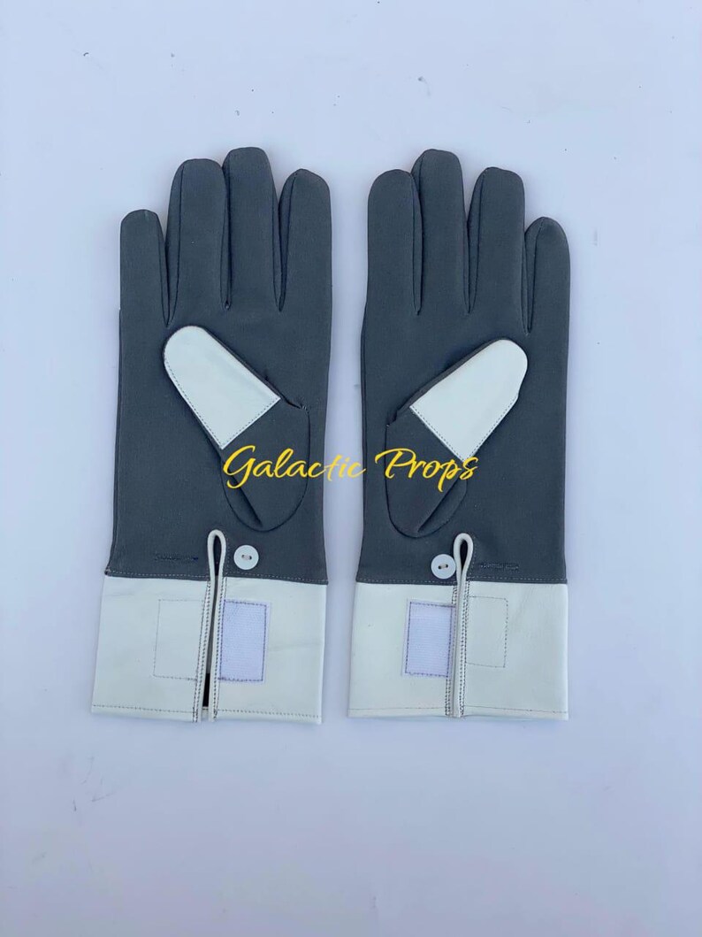 May include: A pair of gray gloves with white accents. The gloves have a white cuff and a white patch on the back of the hand. The text "Galactic Props" is printed on the gloves.