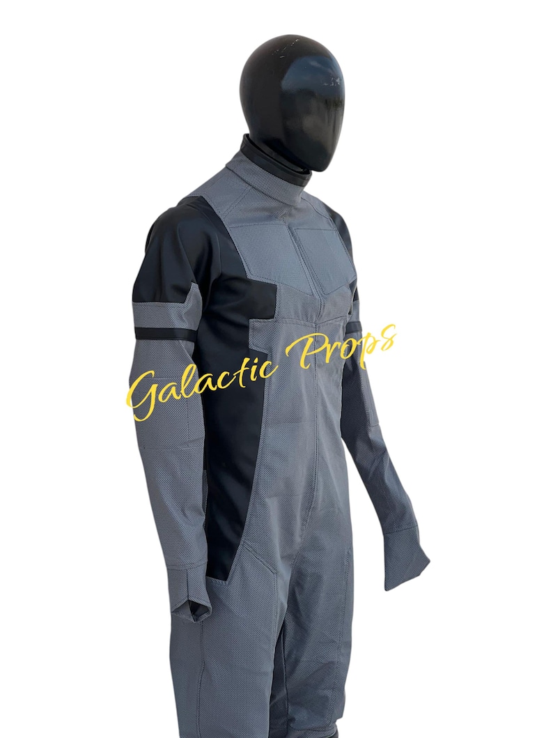 May include: A gray and black jumpsuit with a high collar and long sleeves. The jumpsuit has a textured pattern and is displayed on a mannequin. The text "Galactic Props" is visible in yellow script.