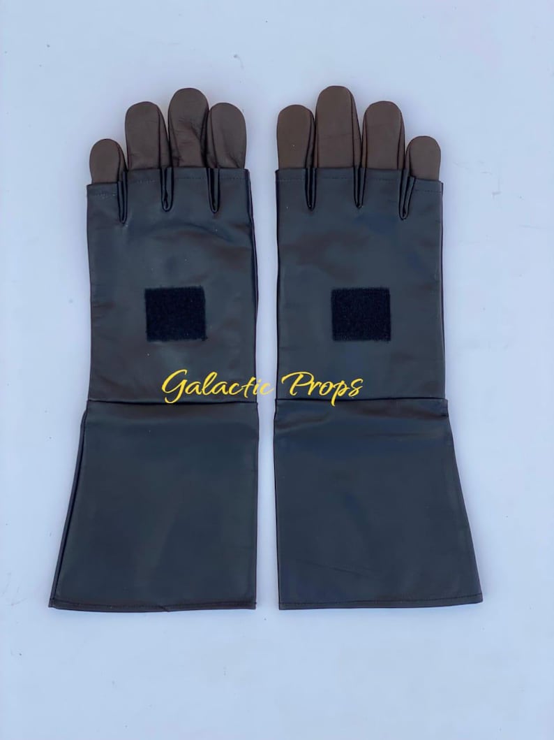 May include: A pair of black gloves with brown fingertips and a black square patch on the wrist area. The gloves have long sleeves and the text "Galactic Props" is visible in gold.