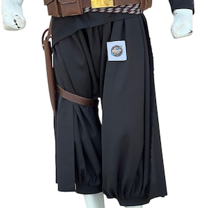 Pu&ograve; includere: Pantaloni neri da costume con caviglia arricciata e fondina in pelle marrone. Una cintura marrone e dorata con fibbia dorata &egrave; indossata in vita. Il testo "Galactic Props" &egrave; su un piccolo adesivo sui pantaloni.