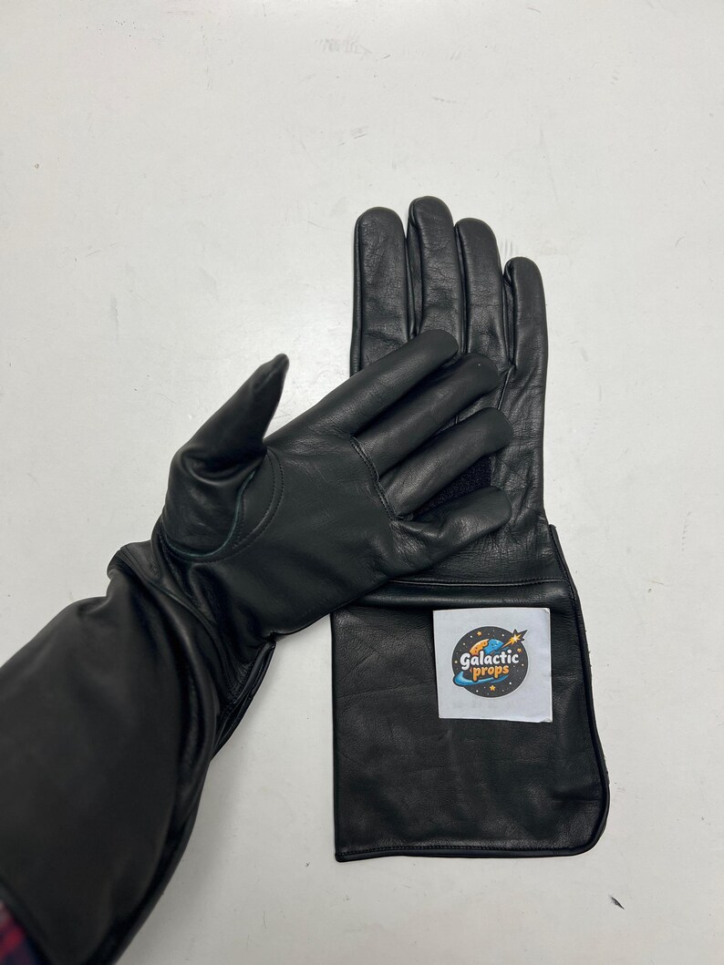 May include: Black leather gloves with long gauntlets. The gloves have a smooth texture and are designed for protection. A white label with the text "Galactic Props" is attached to the gauntlet.