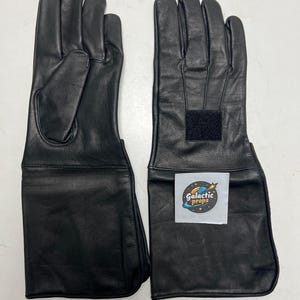 May include: A pair of black leather gloves with extended cuffs. The gloves have a smooth texture and a velcro fastening on the cuff. The gloves are designed for protection, possibly for a costume or work.