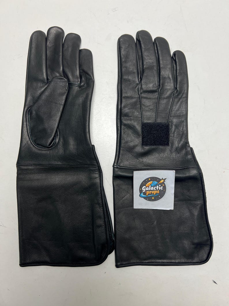 May include: A pair of black leather gloves with extended cuffs. The gloves have a smooth texture and a velcro fastening on the cuff. The gloves are designed for protection, possibly for a costume or work.
