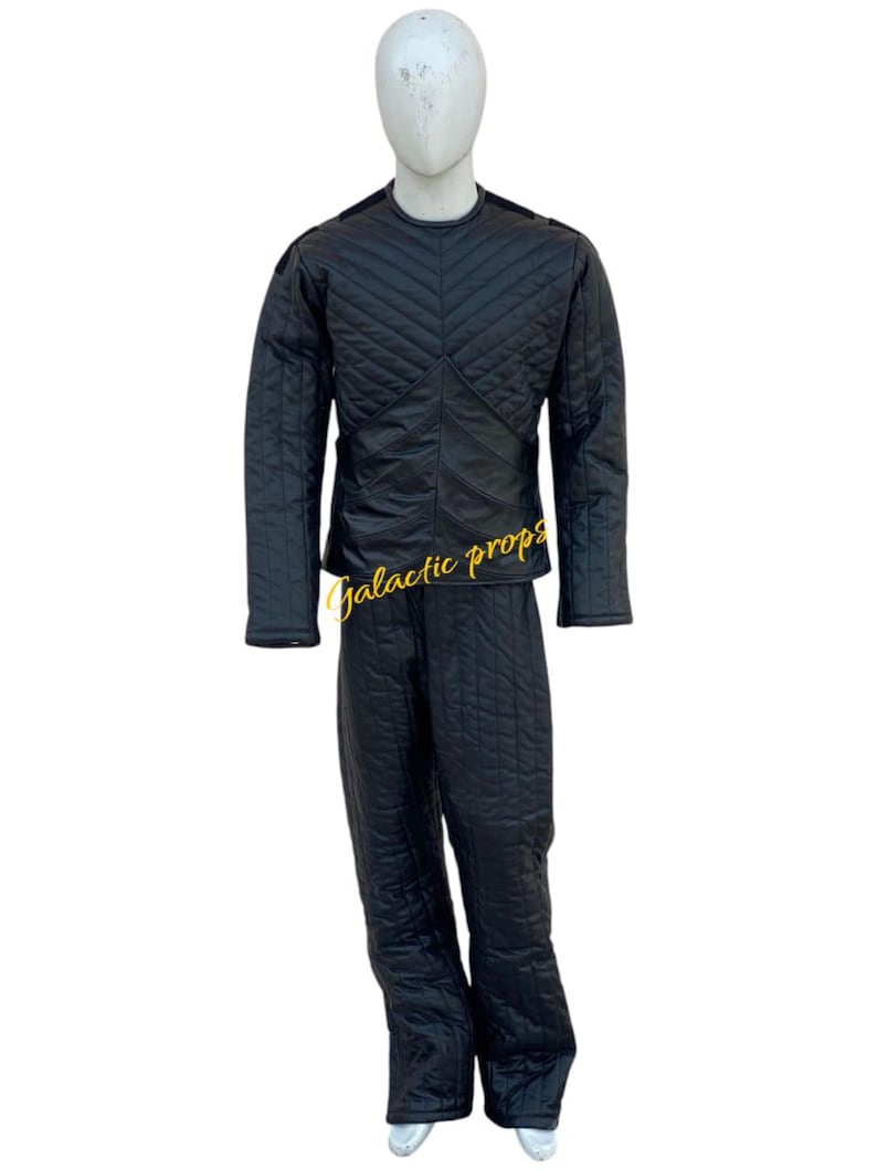 Puede incluir: Un mono negro acolchado con un patr&oacute;n de diamante. El mono tiene mangas largas y un cuello alto.
