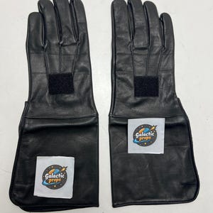 May include: A pair of black leather gloves with extended cuffs. Each glove has a rectangular velcro patch on the back of the hand and a white sticker with the text "Galactic Props".
