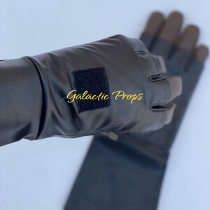 May include: Black fingerless gloves with brown fingertips. The gloves have a rectangular black velcro patch and the text "Galactic Props" in gold script. The gloves are made of a shiny material.