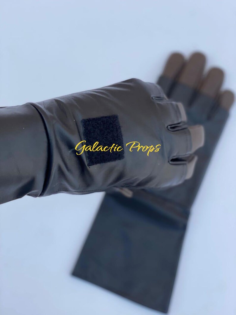 May include: Black fingerless gloves with brown fingertips. The gloves have a rectangular black velcro patch and the text "Galactic Props" in gold script. The gloves are made of a shiny material.