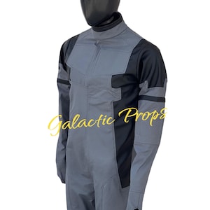 May include: A gray and black jumpsuit with the text "Galactic Props" in a gold script. The jumpsuit has a high collar, long sleeves, and a textured pattern on the front and sleeves. The mannequin head is black.