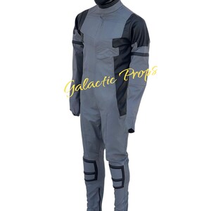 May include: A gray and black jumpsuit with the text "Galactic Props". The jumpsuit features a high collar, long sleeves, and reinforced knee pads. The mannequin is wearing black boots.