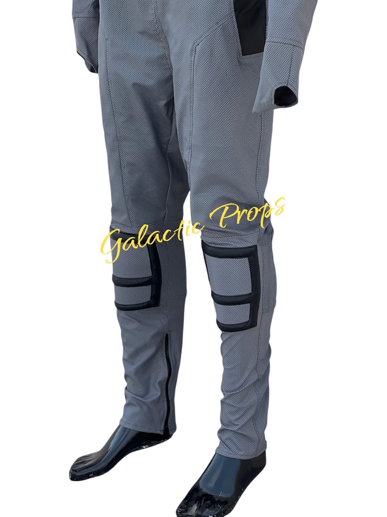 May include: Gray jumpsuit with black accents, featuring knee pads and zippers. The text "Galactic Props" is visible in a gold script. The jumpsuit appears to be made of a textured fabric, possibly for a costume or cosplay.