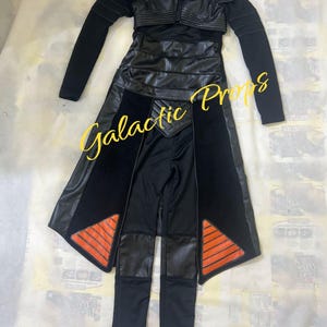 May include: Black costume comprising a faux leather jacket, skirt, and trousers. The jacket features a collar and zip. The skirt and trousers have orange detailing. Ideal for cosplay or themed events.