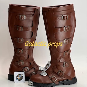 May include: Brown leather boots with multiple buckles and straps. The knee-high boots have a black sole and metal accents. The boots have the text "Galactic props" on them.