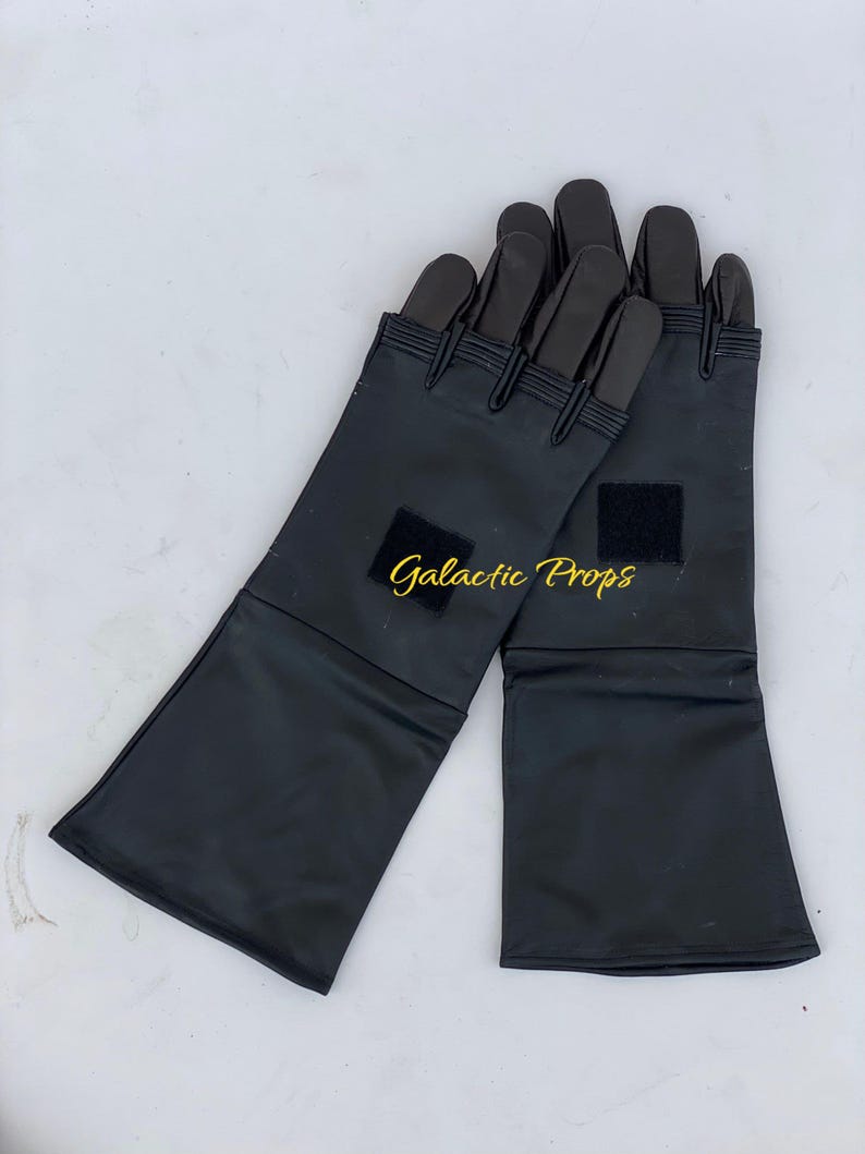 May include: A pair of black gloves with long cuffs. The gloves have a smooth, shiny texture and feature a small square patch on each cuff. The fingers are segmented and reinforced. The text "Galactic Props" is visible in the image.