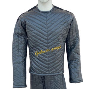 Puede incluir: Un mono negro acolchado con un dise&ntilde;o en forma de V en la parte delantera. El mono tiene mangas largas y cuello redondo. El texto "Galactic Props" est&aacute; bordado en amarillo en la parte delantera.