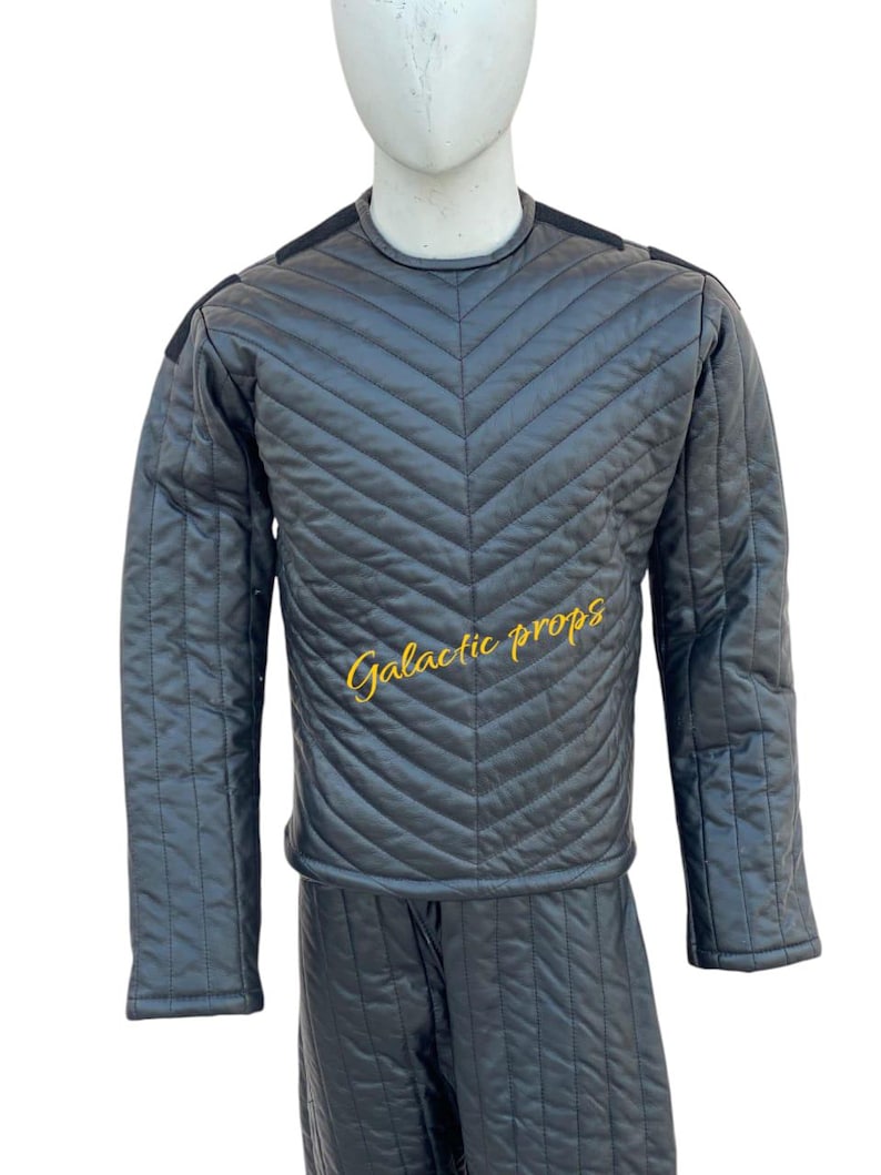 Puede incluir: Un mono negro acolchado con un dise&ntilde;o en forma de V en la parte delantera. El mono tiene mangas largas y cuello redondo. El texto "Galactic Props" est&aacute; bordado en amarillo en la parte delantera.