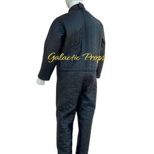 May include: Black quilted jumpsuit with vertical stitching, displayed on a mannequin. The jumpsuit has a high collar, a full-length zipper, and matching pants. The text "Galactic Props" is visible in gold script.