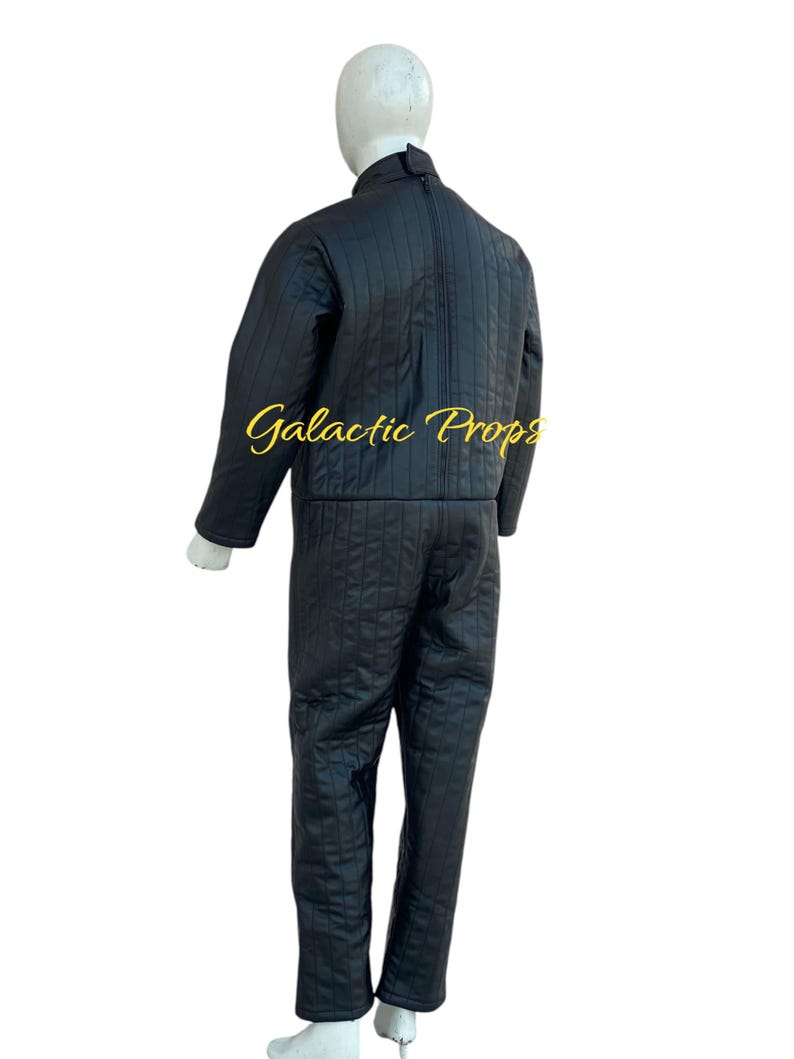 May include: Black quilted jumpsuit with vertical stitching, displayed on a mannequin. The jumpsuit has a high collar, a full-length zipper, and matching pants. The text "Galactic Props" is visible in gold script.