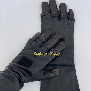 May include: Black leather gloves with a long cuff and reinforced fingers. The gloves have a textured appearance and a Velcro patch on the wrist. The text "Galactic Props" is visible in gold lettering.