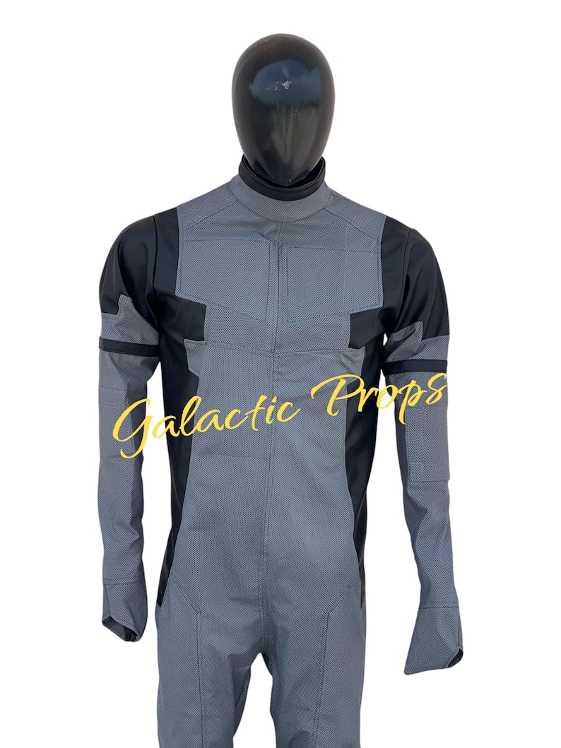 May include: A gray and black jumpsuit with a high collar and long sleeves. The jumpsuit has a textured pattern on the front and sleeves, with black panels on the shoulders and sides. The text "Galactic Props" is written in a cursive font.