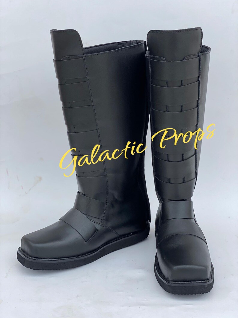May include: Pair of black knee-high boots with multiple straps and a square toe. The boots have a smooth, matte finish and are displayed on a white surface. The text "Galactic Props" is visible in the image.