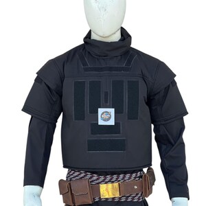 Pu&ograve; includere: Gilet tattico nero con pi&ugrave; pannelli e collo alto, esposto su un manichino. Il gilet presenta una cintura marrone con tasche e una fibbia dorata. Le maniche sono lunghe e nere.