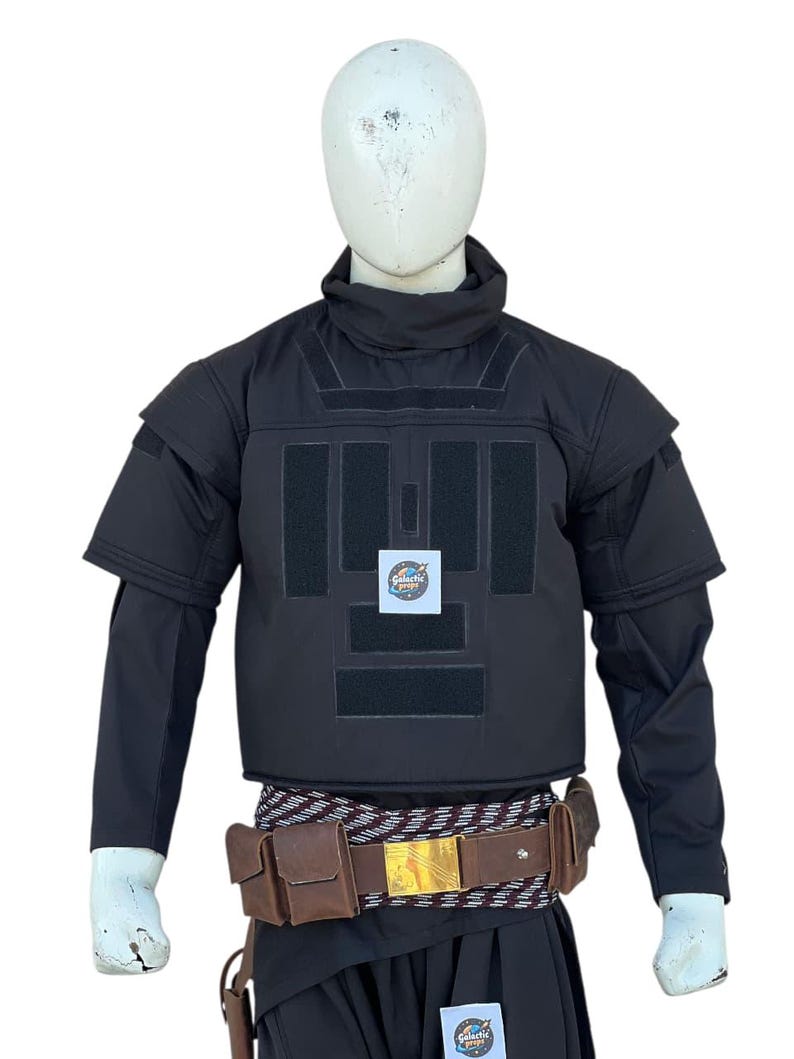 Pu&ograve; includere: Gilet tattico nero con pi&ugrave; pannelli e collo alto, esposto su un manichino. Il gilet presenta una cintura marrone con tasche e una fibbia dorata. Le maniche sono lunghe e nere.