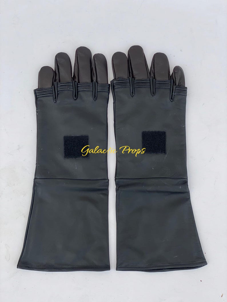 May include: A pair of black gloves with long cuffs, featuring a rectangular black patch on each. The gloves have a segmented design on the fingers and are likely made of a synthetic material. The text "Galactic Props" is visible.
