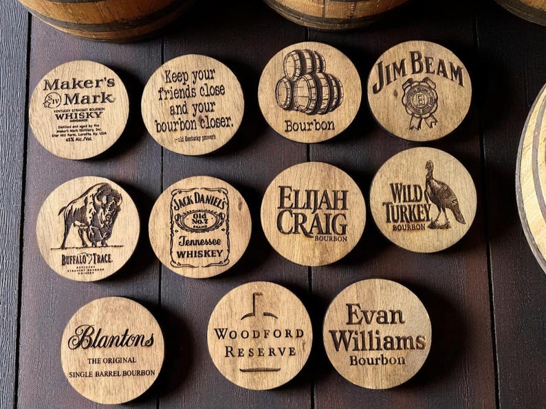 May include: A collection of wooden coasters with various bourbon and whiskey brand logos and slogans, including "Maker's Mark," "Jim Beam," and "Buffalo Trace." The coasters are round and made of light-colored wood.