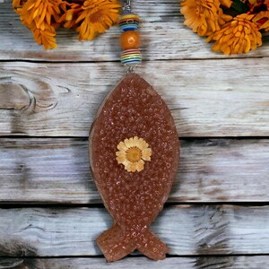 May include: A brown fish-shaped ornament with a pressed dried flower inside. The ornament is hanging from a string of colourful beads.