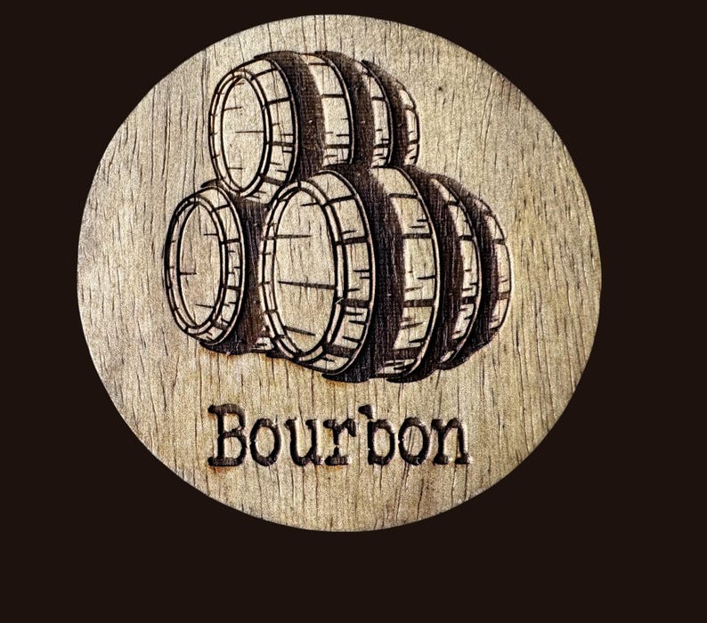 May include: A round wooden coaster with a laser-etched design of bourbon barrels. The word "Bourbon" is etched below the barrels. The coaster is made of light-colored wood and has a dark brown background.