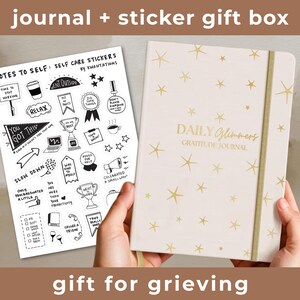 May include: A journal and sticker gift box. The journal is cream-colored with gold star designs and the text "Daily Glimmers Gratitude Journal." The sticker sheet includes self-care themed illustrations and text. The text at the top says "journal + sticker gift box" and "gift for grieving."