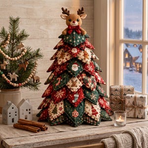 May include: A fabric Christmas tree decoration featuring layered, quilted leaves in red and green with festive patterns including Santa, gingerbread men, snowflakes, and reindeer. A plush reindeer topper with a red bow sits at the very peak.