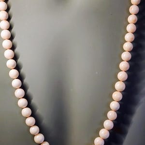 May include: A necklace made of pale pink coral beads. The beads are round and smooth, and the necklace is strung on a thin cord.