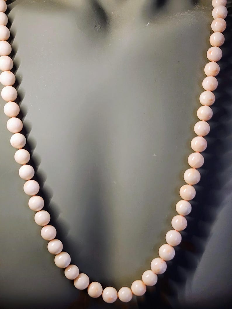 May include: A necklace made of pale pink coral beads. The beads are round and smooth, and the necklace is strung on a thin cord.