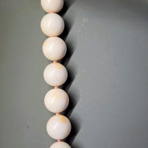 May include: A strand of white coral beads with a pink thread running through them.
