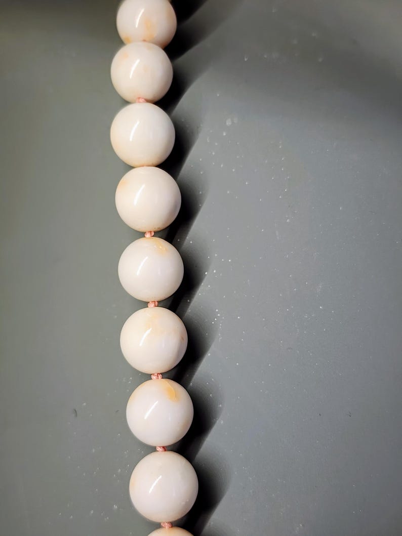 May include: A strand of white coral beads with a pink thread running through them.