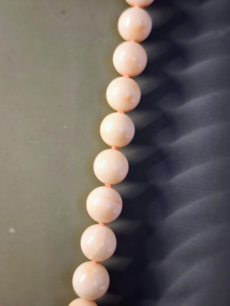 May include: A strand of pale pink coral beads strung together with a thin pink cord. The beads are round and smooth, and they have a slightly iridescent sheen.