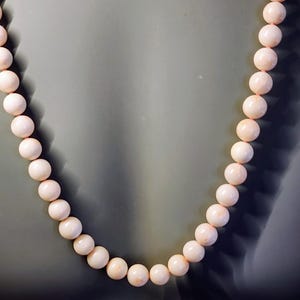 May include: A necklace made of pale pink coral beads. The beads are round and smooth, and the necklace is strung on a thin cord.