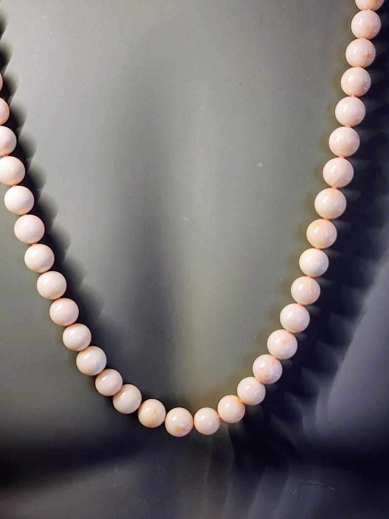 May include: A necklace made of pale pink coral beads. The beads are round and smooth, and the necklace is strung on a thin cord.