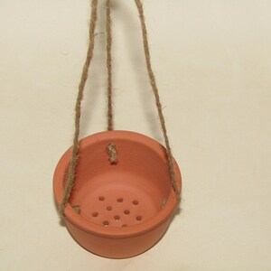 May include: A terracotta hanging planter with drainage holes and a natural twine rope.