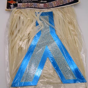Puede incluir: Una pancarta de cumpleaños empaquetada con las palabras "HAPPY BIRTHDAY" en rosa y dorado. La pancarta es azul con detalles de purpurina plateada y está empaquetada con flecos beige. La pancarta mide 2,7 m de largo.