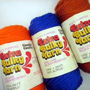 May include: Three skeins of yarn in orange, blue, and brown. Each skein has a label that reads "Multi-Purpose Extra Bulky Yarn" with the text "Easy Care Mildew Resistant" and "3 Ply 210 ft. 100% Acrylic".