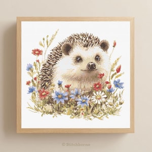May include: A framed cross-stitch of a hedgehog surrounded by colorful wildflowers. The hedgehog has a light brown face and dark brown quills. The flowers are red, blue, and white, with green foliage. The frame is made of light-colored wood.
