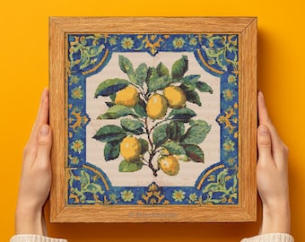 May include: A framed cross-stitch artwork depicting a lemon tree with yellow lemons and green leaves. The artwork is set within a blue and gold decorative border and a light brown wooden frame. The artwork is held by two hands.